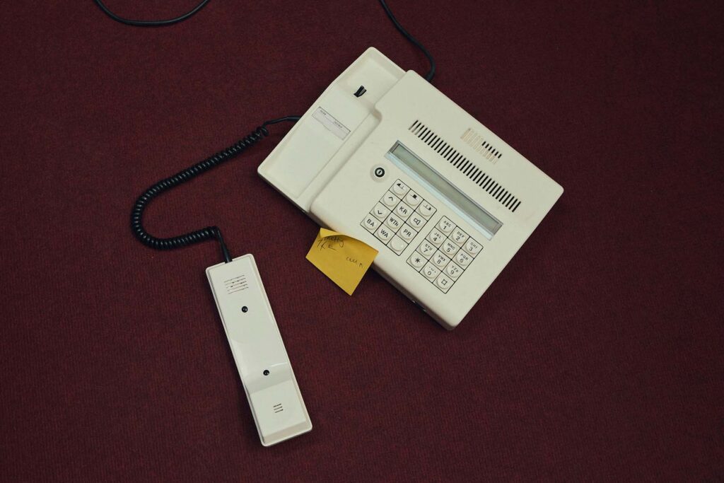 A telephone off its receiver with a yellow sticky note